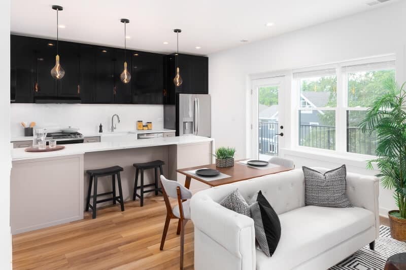 A beautiful renovated kitchen with black and brown cabinets and white granite waterfall countertops. A living and dining room sit in front of the kitchen.
